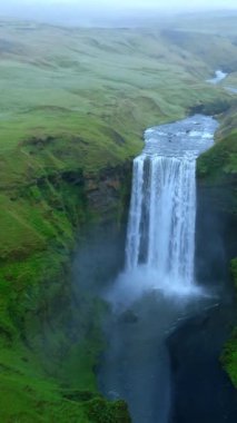 Görkemli hava manzarası, geniş yeşil bir arazide akan güçlü bir Skogafoss şelalesinin sularının arazide dramatik bir yol açtığını gösteriyor. İzlanda, Skogar. 