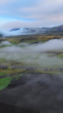 Büyüleyici bir hava manzarası İzlanda 'nın yemyeşil tarlalarında ve uzak dağlarında süzülen bulutları gösteriyor İzlanda dağlarının dingin ve ruhani özünü gözler önüne seriyor. İzlanda. 