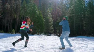 Neşeli Afrikalı Amerikalı çift Yosemite Ulusal Parkı 'ndaki yumuşak karda oynuyorlar. Uzun yeşillikler ve çarpıcı kış manzaralarıyla çevrili. Açık havada eğlenmek ve gülmek için mükemmel bir ortam yaratıyorlar.