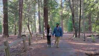 Sevgi dolu çift, Yosemite Ulusal Parkı 'nın manzaralı patikalarında el ele yürürken, kışın yeryüzüne getirdiği yüksek ağaçlar ve nefes kesen doğal güzelliklerle çevrelenir.