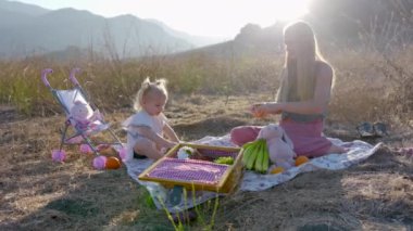 Sevgi dolu bir anne, küçük kızıyla piknikte kaliteli zaman geçirir. Güzel bir dağ zeminine karşı kurulur. Aile bağı kurmak ve doğanın tadını çıkarmak için mükemmel bir ortam yaratır.