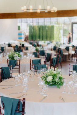 Zarif bir düğün resepsiyonunda, bu neşeli olay için mükemmel romantik bir ortam yaratan, sıcak ışıkla güçlendirilmiş, çarpıcı çiçek süslemeleri olan güzel masalar bulunur.