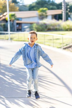 Aydınlık ve güneşli bir günde, neşeli genç bir çocuk rahat bir yolda yürüyor, rahat kot ve canlı renkler giyiyor, mutluluğu somutlaştırıyor ve etrafa bulaşıcı enerji saçıyor.