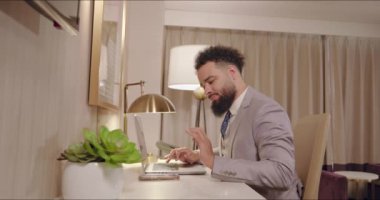 Sivri takım elbiseli neşeli Afro-Amerikan işadamı telefonuna odaklanırken aynı zamanda şık ve şık bir otel odasında, profesyonellik ve modernlik üzerine çalışıyor.