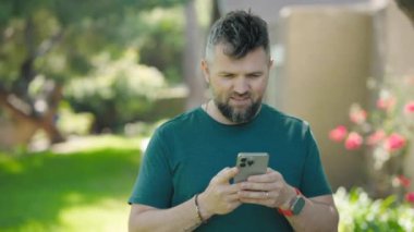 Bir adam akıllı telefonuyla çevresi yemyeşil yemyeşil ve çiçeklerle çevriliyken dijital dünyasına bağlı kalarak doğanın güzelliğinin tadını çıkarıyor.