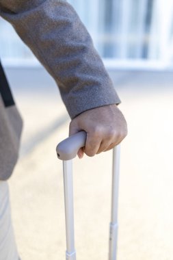 Sivri takım elbiseli bir Afro-Amerikan işadamı elinde parlak bir bavul tutarak, güçlü kariyer hırslarını ve isteklerini yansıtan seyahat veya önemli bir yolculuğa hazır olduğunu öne sürüyor.