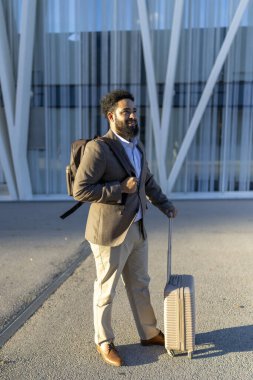 Zarif bir bavul tutan şık bir işadamı, modern bir mimari binanın önünde duruyor, profesyonellik, entelektüellik, seyahat ve iş girişimlerine hazırlık.