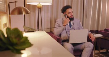 Son derece profesyonel iş adamı, modern dekor ve tasarım sergileyen şık bir ofis ortamında dizüstü bilgisayarı üzerinde çalışırken aktif olarak odaklanmış bir telefon görüşmesi yapıyor.
