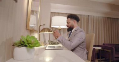 İyi giyimli bir adam modern bir ofiste düzgün bir masada oturmakta, akıllı telefonuna odaklanmış, profesyonellik, verimlilik ve üretkenlik saçan sakin bir atmosferde çalışmaktadır.