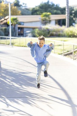 Rahat ve rahat kıyafetler giyen neşeli ve mutlu bir çocuk, güneşli bir parktaki güzel bir yolda enerjik bir şekilde koşuyor. Gün boyunca sınırsız enerji ve heyecan yayıyor.