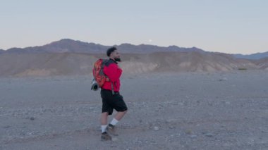 Ölüm Vadisi 'nde, canlı kırmızı ceketli bir turist bir sırt çantası taşır ve etraflarını saran engin, açık çölün enfes doğal güzelliğinin tadını çıkarır.