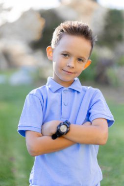 Parlak mavi polo tişört giymiş neşeli genç bir çocuk yemyeşil bir açık hava ortamında, neşeli bir ruh yayıyor ve hayata karşı kaygısız tavrını sergiliyor.