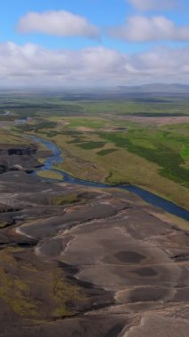 Engebeli İzlanda manzarasının geniş hava manzarasında volkanik ovalarda dönen bir nehir ve berrak mavi gökyüzünün altındaki yemyeşil alanlar görülüyor. Macera meraklıları. İzlanda. 