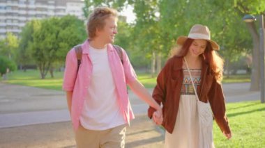 Güneşli, enerjik bir parkta el ele gezen genç bir çift, mutluluğun özünü vurgulayan güzel bir manzara içinde saf neşe ve derin aşk yayıyor.