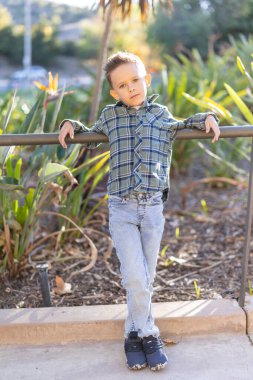 Genç bir çocuk, çevresi canlı yeşilliklerle çevriliyken, rahat bir şekilde dışarıda poz veriyor. Bu da sahneyi güzelleştiriyor. Bu görüntü aile, yaşam tarzı ya da moda teması için mükemmeldir.