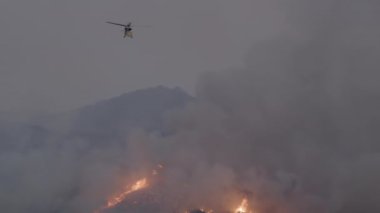 Bir helikopter Los Angeles yakınlarındaki orman yangınlarıyla aktif olarak mücadele ediyor, yakındaki evleri tehdit eden ve hayatları tehlikeye atan bu tehlikeli yangınla mücadele etmek için acil çabaları vurguluyor.
