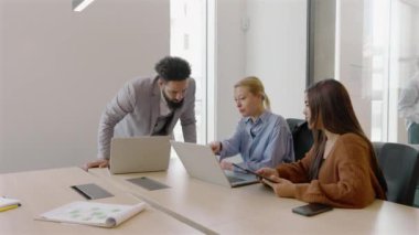 Yoğunlaştırılmış takım toplantısı modern ve şık bir ofis ortamında, çeşitli profesyoneller laptopları etkin bir şekilde kullanırken görevlerini aktif olarak yerine getiriyorlar.