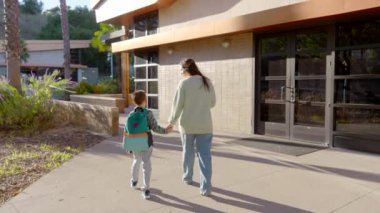 Dokunaklı ve iç açıcı bir sahne, sevgi ve şefkat dolu, aydınlık bir günde, modern bir binaya doğru el ele yürüyen sevgi dolu bir anne ve küçük çocuğunu tasvir eder.