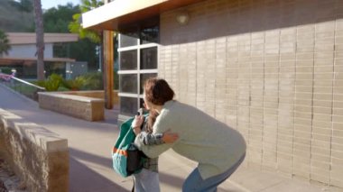 Güzel, güneşli bir açık hava ortamında, kendini adamış bir ebeveyn uzun bir okul gününden sonra yorulmuş çocuğunu sıcak bir şekilde kucaklar, derin bir sevgi ve kalpten gelen derin bir bağla dolu gerçekten önemli bir anı yakalar.