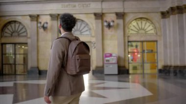 Meşgul bir tren istasyonu lobisinde, Afrikalı bir Amerikalı işadamı güvenli bir şekilde yürür, parlak bir şekilde gülümser, akıllı bir telefonu dengeler ve seyahat çantası taşır, yolculuk için hazır ve heyecanlıdır.