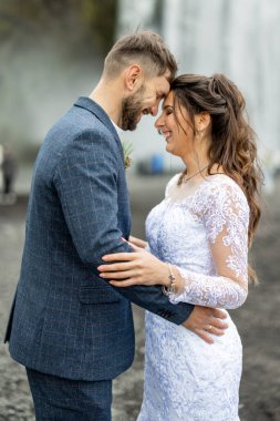 Güzel bir düğün çifti, bu unutulmaz anda birbirlerine sevgilerini, mutluluklarını ve bağlılıklarını gösteren nefes kesici bir şelalenin yanında neşeyle kucaklaşır.