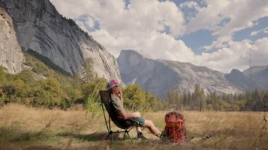 Bir adam bir sandalyede rahatça dinlenmek için bir dakikasını ayırır, yanında sırt çantasıyla dinlenir, hepsi Yosemites 'in nefes kesici ve görkemli manzarasına karşı hazırdır.