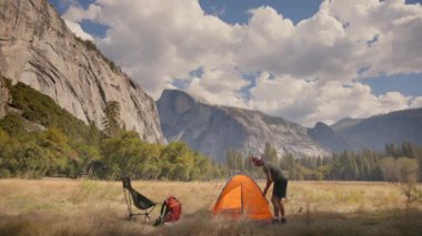 Bir yürüyüşçü, Yosemite Ulusal Parkı 'nın nefes kesici manzarasında canlı turuncu bir çadır kuruyor. Bu çadır, görkemli ve ikonik kaya oluşumlarının yanı sıra barışçıl bir atmosfer içeriyor.