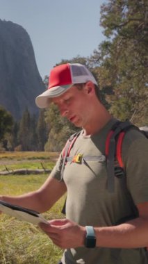 Bir erkek yürüyüşçü, Yosemite Ulusal Parkı 'nın nefes kesici ve nefes kesici manzaralarını aktif olarak keşfediyor. Elinde detaylı bir harita var. Çevresindeki güzel doğaya tamamen dalmış.