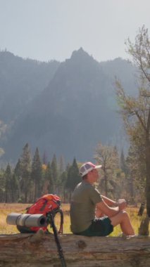 Bir adam nefes kesen Yosemite Milli Parkı 'nda yürüyüş yaparken sakin ve huzurlu bir andan zevk alır. Etrafı çarpıcı, yüksek dağlarla ve doğanın güzelliğiyle çevrilidir.