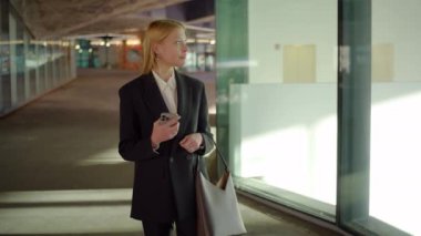 Zarif bir iş elbisesi içinde yetenekli profesyonel bir kadın modern bir ofiste duruyor, akıllı telefonunu kontrol ediyor ve fırsatlar ve zorluklarla dolu verimli bir iş gününe hazırlanıyor.