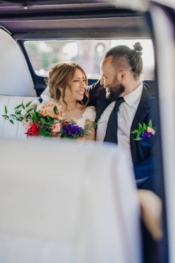 Göz kamaştırıcı derecede güzel bir çift zarif bir düğün kıyafeti giyip etraflarındaki canlı çiçeklerle süslenmiş lüks bir limuzinin içinde hassas ve samimi bir anı paylaşıyorlar.