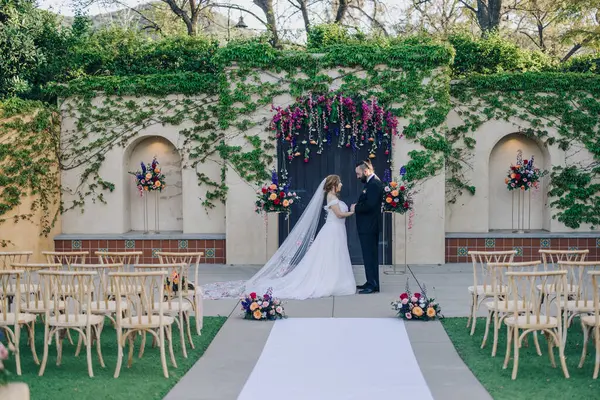 Manzaralı bir yerde, zarif sandalyeler ve yemyeşil çiçeklerle çevrili güzel bir gelin ve damadın romantik bir atmosfer yarattığı açık havada bir düğün töreni.