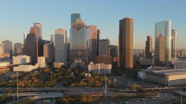 Gün batımında Houston, Teksas şehir merkezinin nefes kesici ve çarpıcı hava manzarası, güzel bir şekilde ikonik gökyüzü ve canlı şehir hayatı sergileniyor. Resmedilmiş ve renkli altın bir zemin.