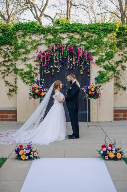 Güzel, büyüleyici bir düğün töreni açık havada düzenlenir. Hoş bir çift, romantik ortamı güzelleştiren çarpıcı çiçek desenleri altında kalpten yeminler eder.