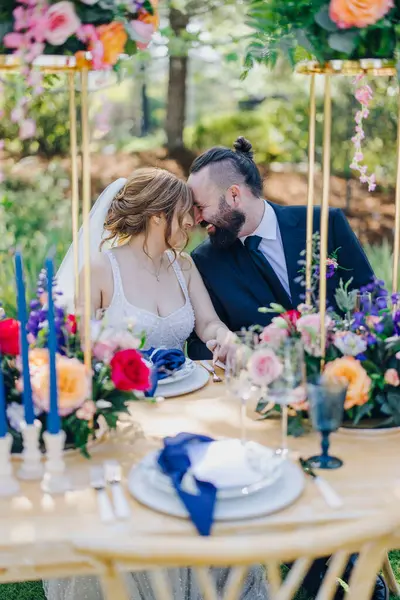 Sevgi dolu bir çift düğün törenlerinde, çiçeklerle ve zarif masalarla çevrili, özel günlerini unutulmaz kılan neşeli bir atmosfer yaratan samimi bir anı paylaşır.