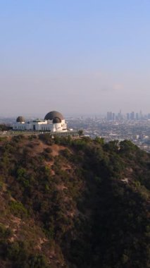 Hollywood Dağı 'ndaki Griffith Gözlemevi' nde gün batımında Los Angeles şehir merkezindeki gökdelenlerin arka planı 4K. Ünlü Los Angeles şehri Kaliforniya ABD