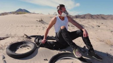 Yalnız bir adam geniş ve kumlu bir çöl manzarasında oturuyor, bir solunum maskesi takıyor, ve atılmış lastik yığınlarıyla çevrili, hepsi güçlü bir post tapokaliptik ve ıssız titreşim uyandırıyor.