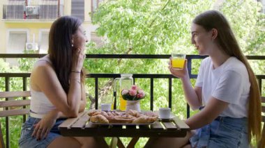 Güzel dişilerin şehir manzarasıyla lezzetli bir kahvaltı ederken yakından çekilmiş görüntüsü. Neşeli, sohbet eden ve içecek içen genç kadınların portresi. Yüksek kalite 4k görüntü