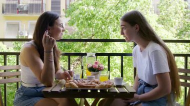 Anne ve kızının açık havada lezzetli ve tatlı hamur işlerinin tadını çıkarırken yakın plan çekimleri. Terasta otururken lezzetli yemek ve içeceklerden keyif alan neşeli kadınların portresi. Yüksek kalite 4k görüntü