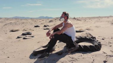 Uçsuz bucaksız ve çorak bir çölde, solunum maskesi takan engebeli bir adam eski lastik yığınlarının arasında oturur, tozla dolu bu ıssız ve vahiysel ortamda hayatta kalma ruhunu somutlaştırır.