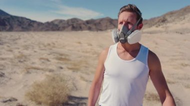 Geniş ve çorak bir çölde, solunum maskesi takan yalnız bir adam, post-kaliptik bir dünyayı somutlaştırıyor, hayatta kalma, izolasyon ve baskın yalnızlık temalarını vurguluyor.