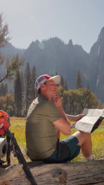 Bir adam, doğayla tamamen çevrili güzel Yosemite Ulusal Parkı 'nda, bir sonraki heyecanlı macerasını dikkatlice planlarken detaylı bir haritaya göz atmak için düşünceli bir an geçirir.