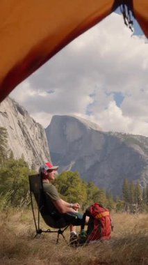 Bir adam Yosemite Ulusal Parkı 'nda huzur ve neşe buluyor, bir çadırın altında dinleniyor ve bu ikonik yeri ziyaret eden herkese korku ve sükunet aşılayan çarpıcı dağ manzaralarının tadını çıkarıyor.