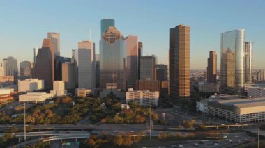 Gün batımında Houston, Teksas şehir merkezinin nefes kesici ve çarpıcı hava manzarası, güzel bir şekilde ikonik gökyüzü ve canlı şehir hayatı sergileniyor. Resmedilmiş ve renkli altın bir zemin.