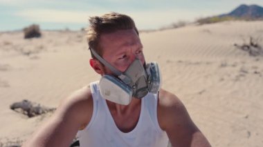 Solunum maskesi takan yalnız bir adam çorak bir çöl manzarasının ortasında oturur. Belirsizlik ve korkuyla dolu sert bir posttapokaliptik dünyada hayatta kalma mücadelesini sembolize eder.