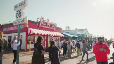 Santa Monica, LOS ANGELES, ABD - 02 Mart 2023: kalabalık insanlar plajda. Tabelanın üstünde fotoğraf çeken bir grup insan. Pier briç burgeri. Güneşli bir gün. Hafta sonu eğlence yaşam tarzı konsepti. Yüksek kalite 4k