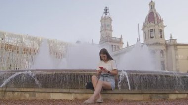 Merdivenlerde otururken akıllı telefonunu kullanan genç bir kızın yakın çekim görüntüsü. Kafkasyalı genç dışarıda sosyal medya iletişiminin keyfini çıkarıyor. Yüksek kalite 4k görüntü