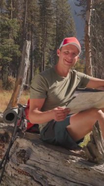 Bir adam inanılmaz Yosemite Ulusal Parkı 'nda doğa tarafından sunulan yüksek ağaçlar ve nefes kesici manzaralarla çevrili bir yürüyüş yaparken hak ettiği dinlenme anını yaşıyor.