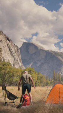 Bir adam Yosemite Ulusal Parkı 'nın nefes kesici ve çarpıcı manzaralarında rahat bir kamp kuruyor. Etrafı görkemli dağlarla çevrili, canlı doğayla dolu ve vahşi doğaya bir kaçış sağlıyor.
