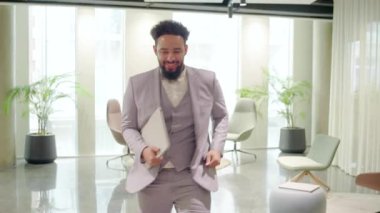 Takım elbiseli kendinden emin bir Afro-Amerikan işadamı canlı bir çalışma alanından geçerek, başarıyı ve profesyonelliği somutlaştırarak, etrafındakilere amaçlarını gerçekleştirmeleri için ilham veriyor.